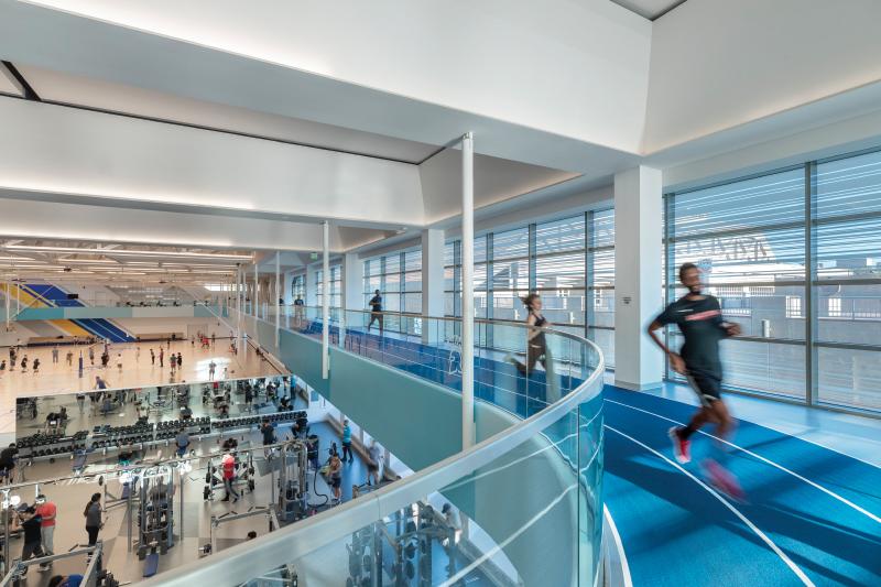 Runners run on 2nd floor track while people lift weights below on the first floor